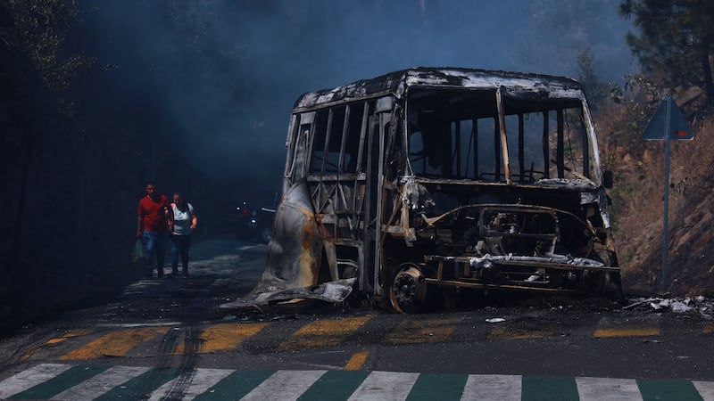 Peatones pasan junto a un autobús calcinado luego de ser incendiado en una carretera de...